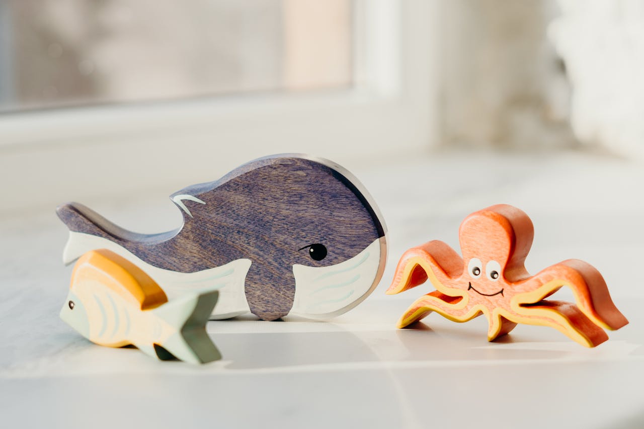 A charming display of wooden toy sea creatures on a bright surface, showcasing a whale, octopus, and fish.