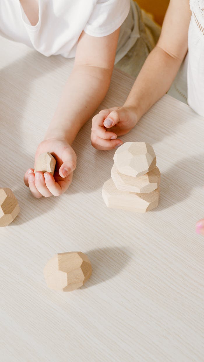 Close-up of kids' hands stacking geometric wooden blocks on a table.